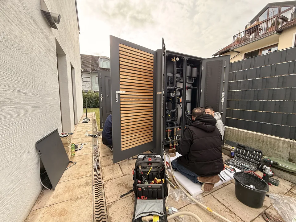 Zwei Techniker arbeiten an der geöffneten Einheit neben dem Haus