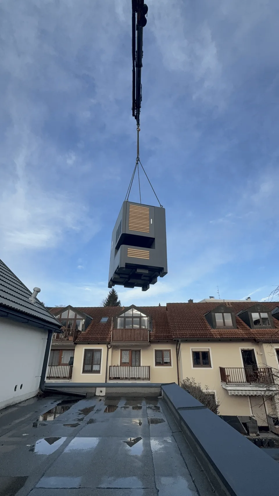 Die verpackte Einheit hängt am Kranhaken über den Dächern